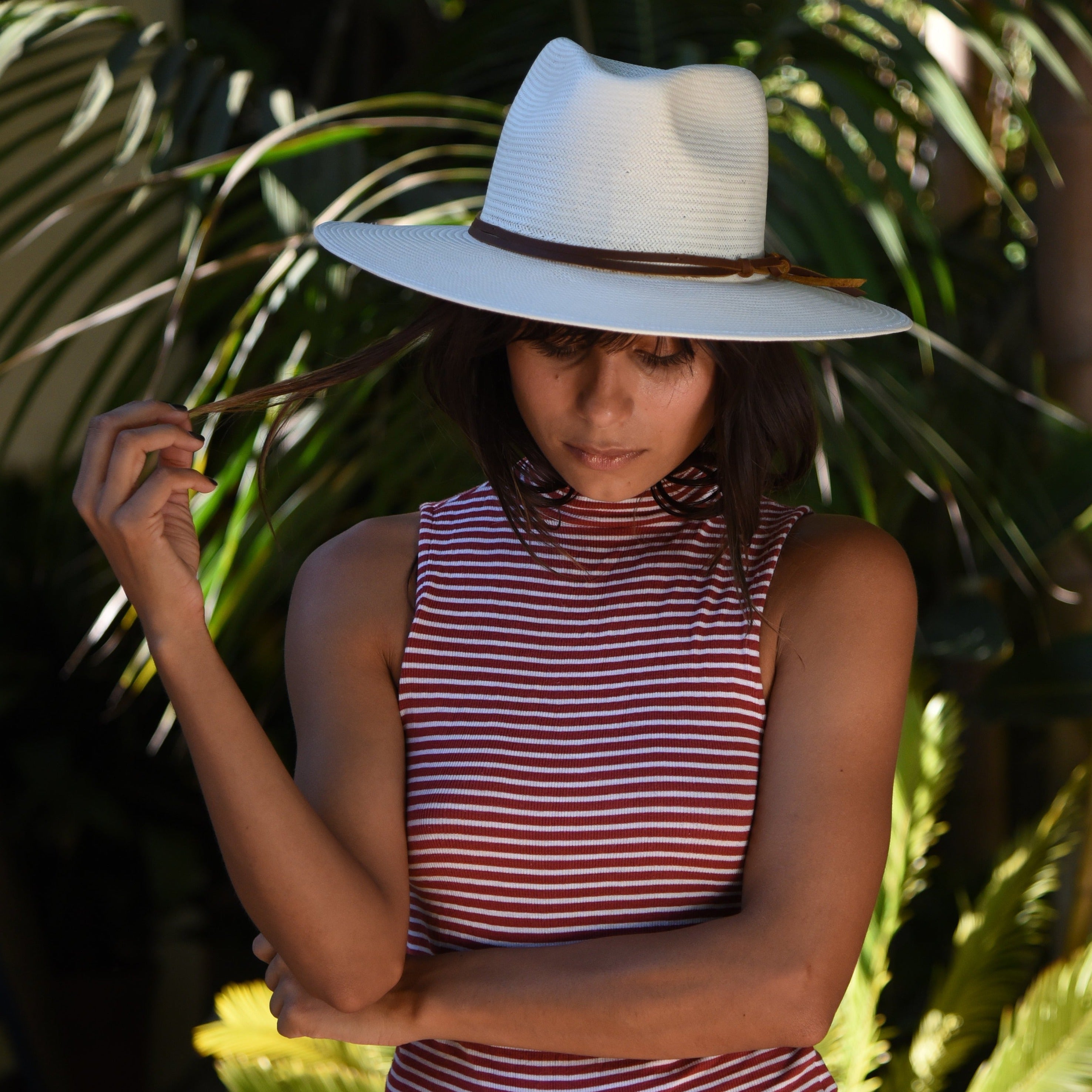 Woman wearing a white sun hat and red and white striped dress standing among green plants.