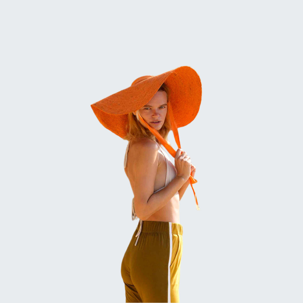 Woman wearing an orange hat and yellow pants standing on rocky terrain.