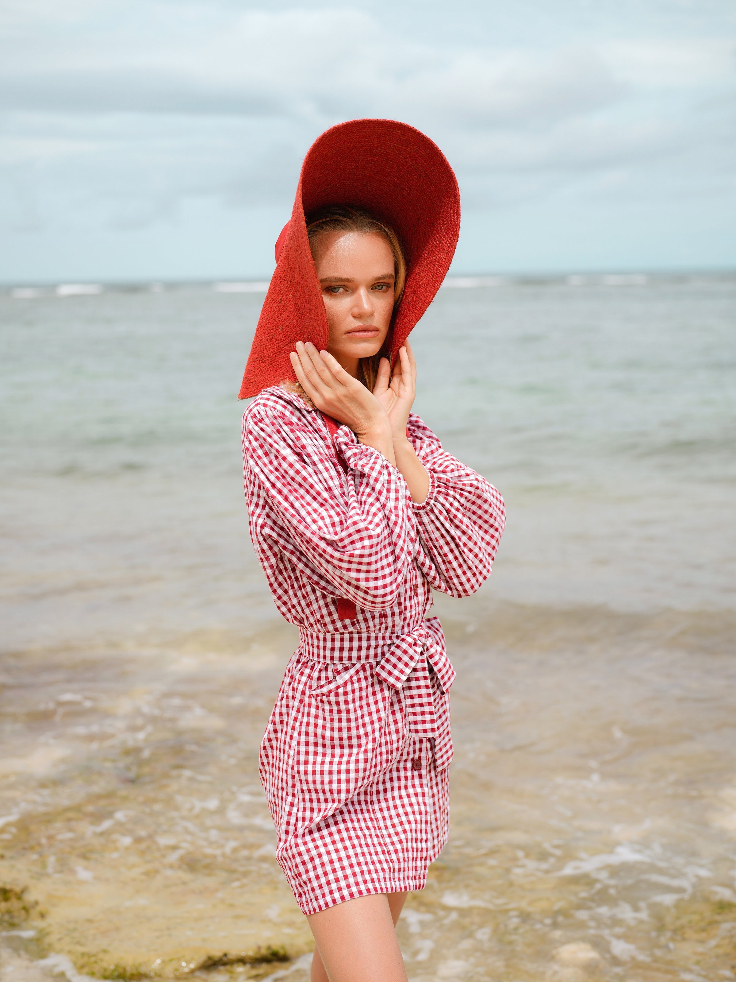 Woman wearing a red checkered dress and red hooded coat on a beach