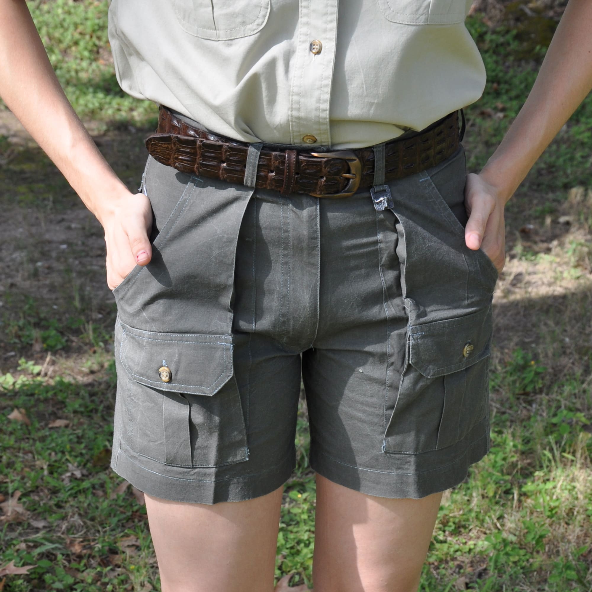 Person wearing gray shorts with multiple pockets and a belt, standing in a natural setting.