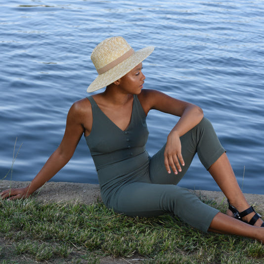 Woman in a green outfit and straw hat sitting by a body of water.