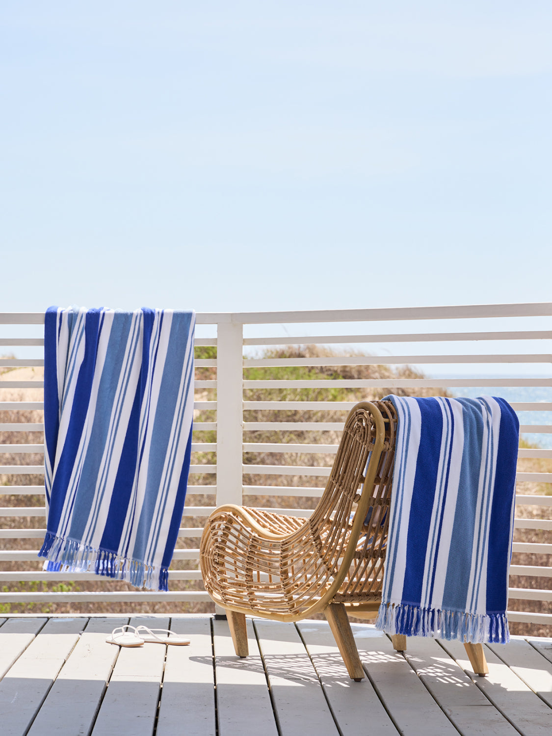 Blue and white striped towel draped over a wicker chair on a wooden deck with a clear blue sky.