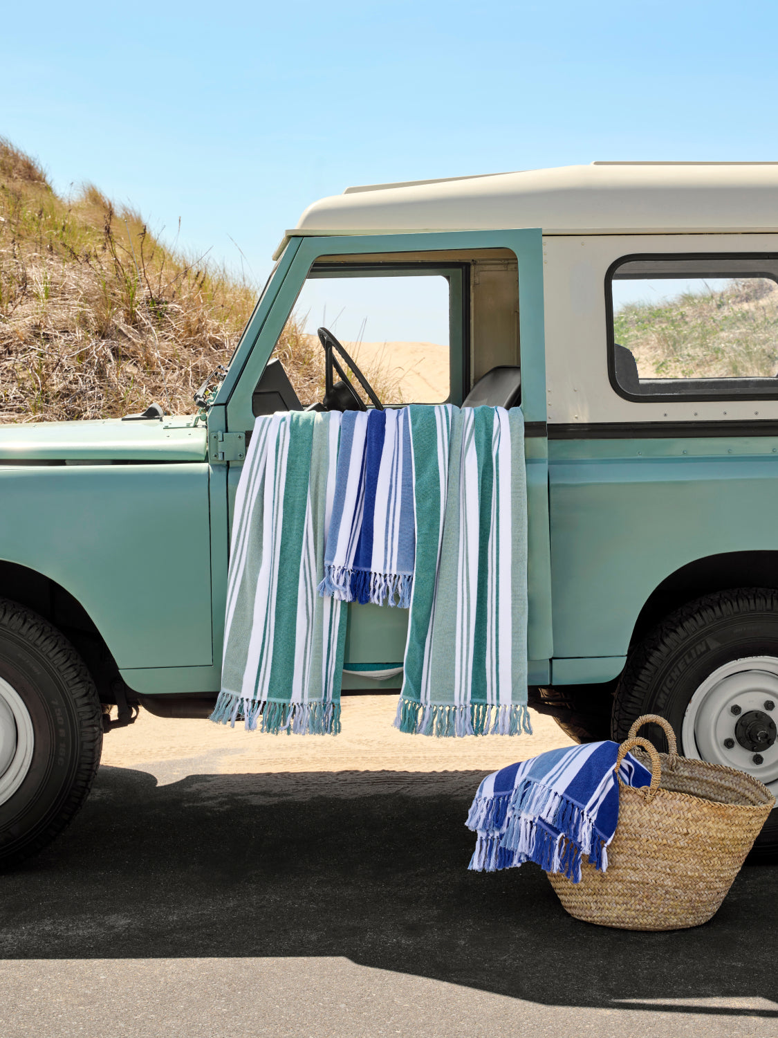Vintage teal truck with striped towels hanging out the window on a beach.