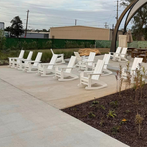 White chairs arranged on a concrete patio with a building and trees in the background