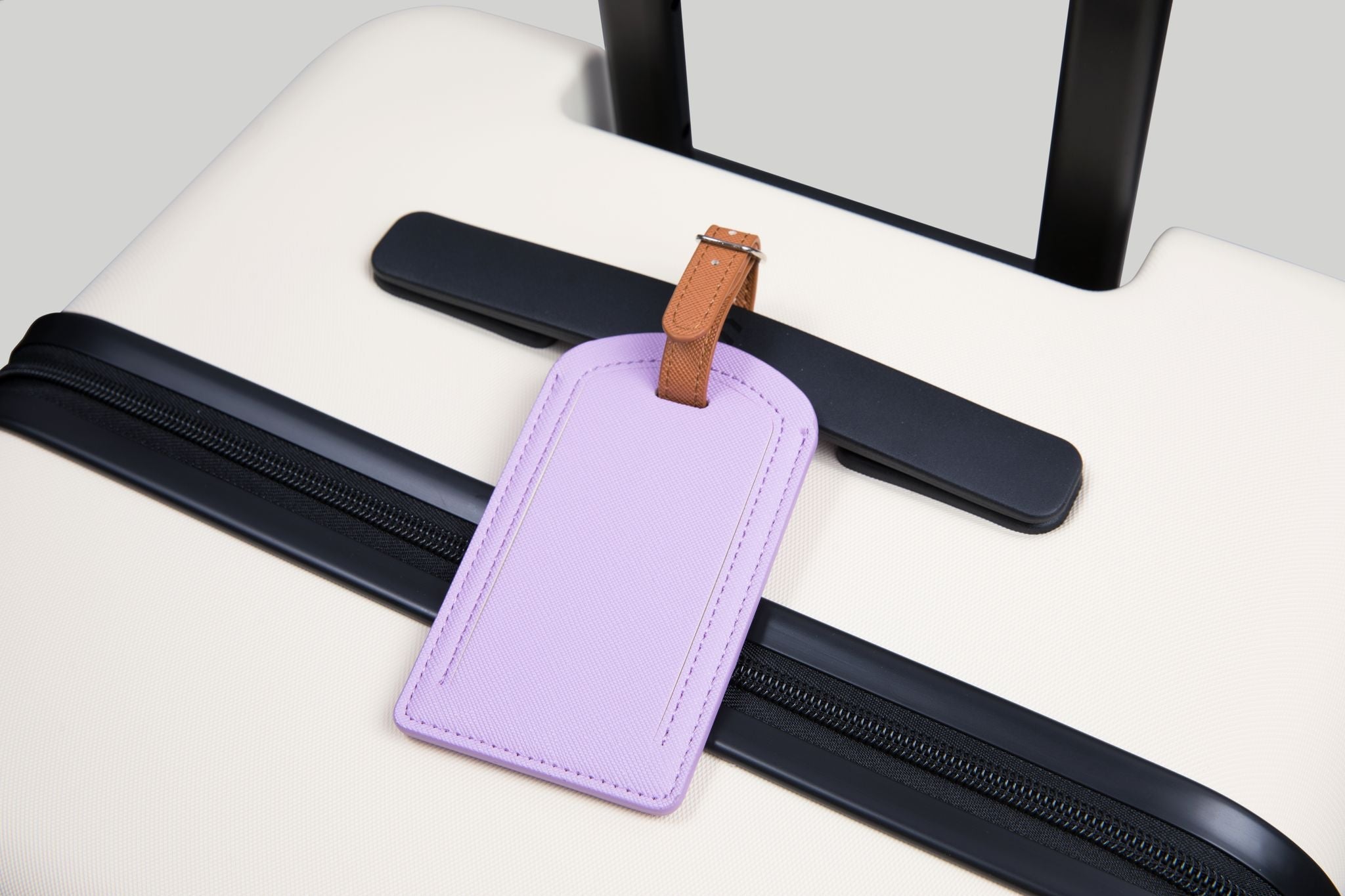 Purple luggage tag with brown strap on a black suitcase handle