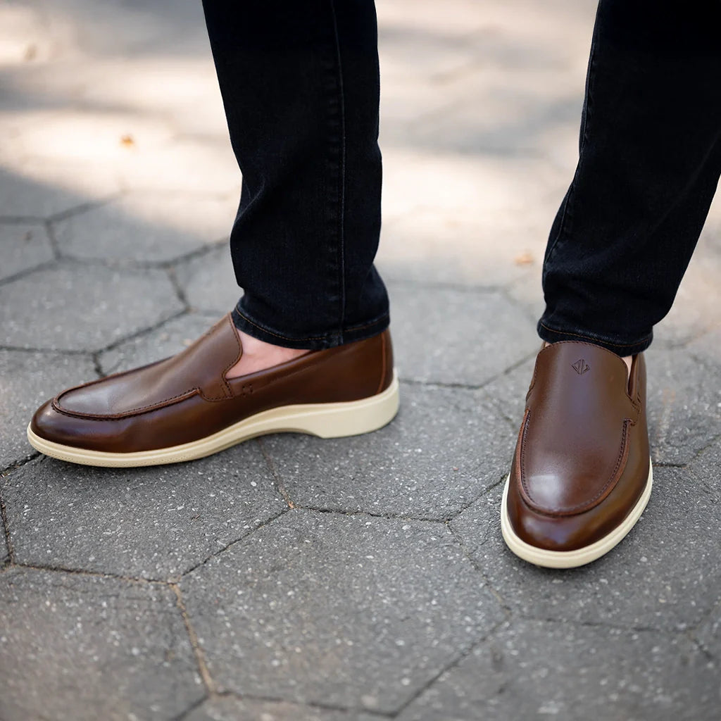 Brown loafers worn with black pants on a stone pavement