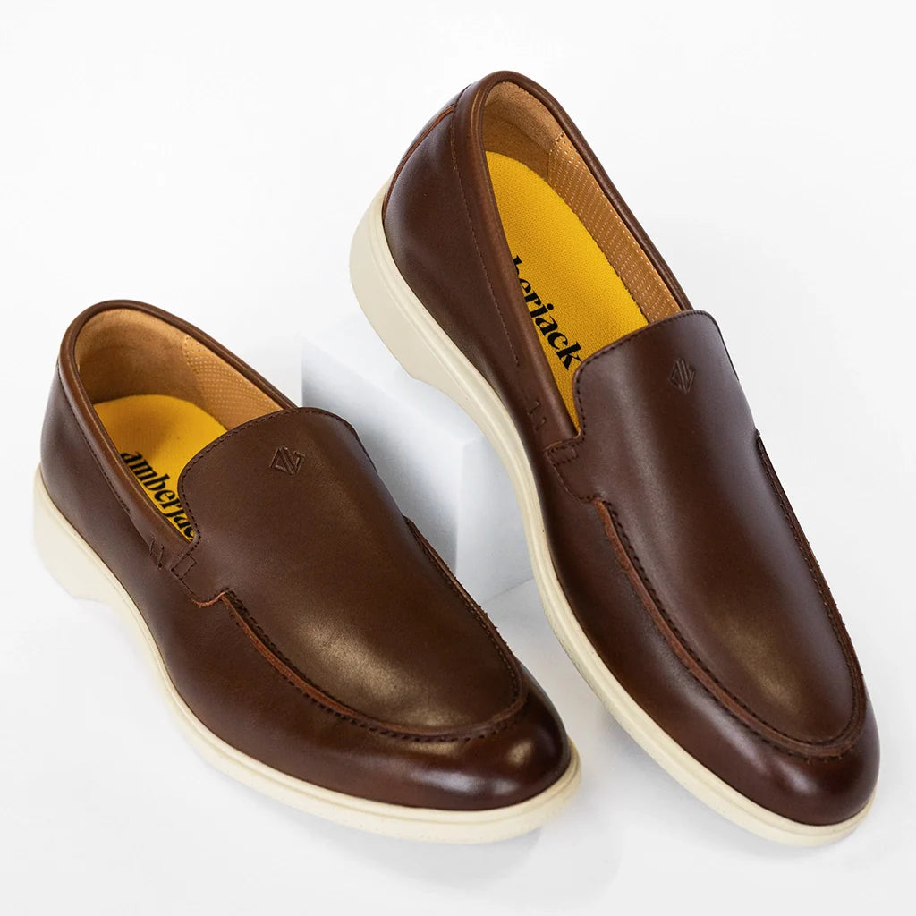 Pair of brown loafers with white soles on a light gray background