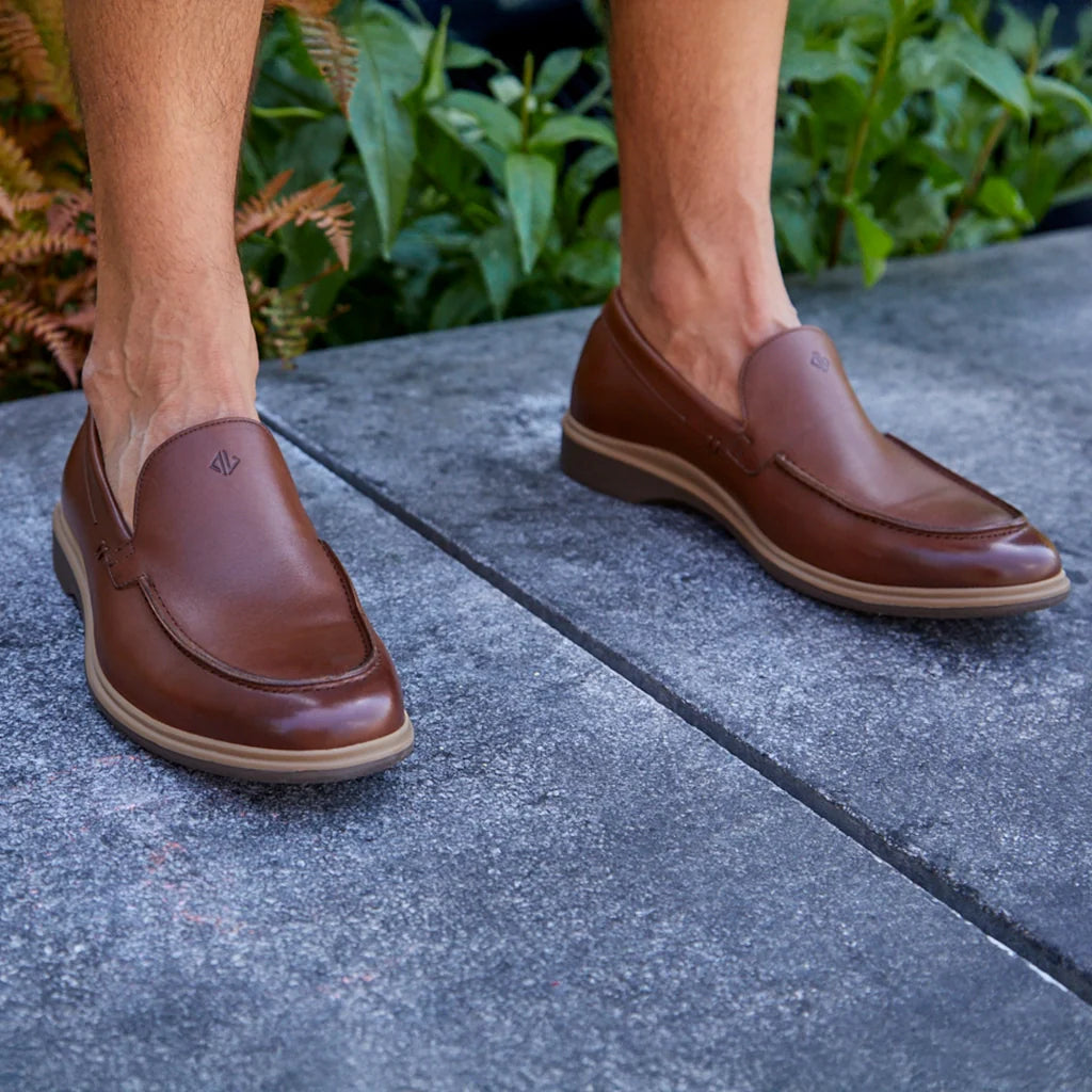 Brown loafers worn on a stone surface with greenery in the background