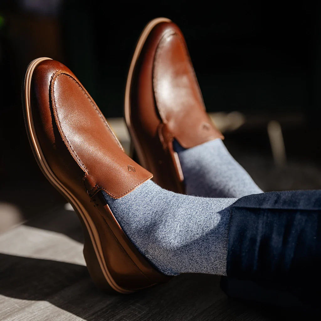 Brown leather loafers worn with blue socks on a blurred background