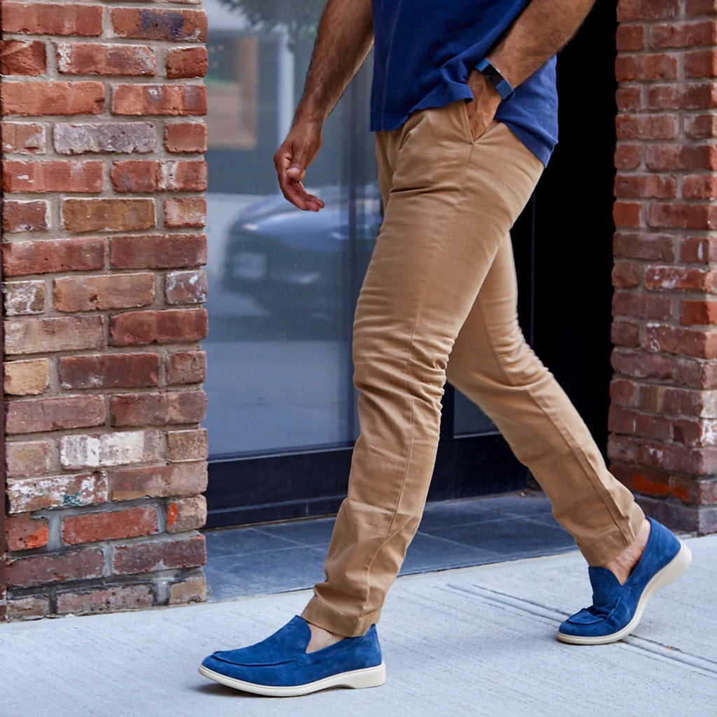 Person wearing tan pants and blue shoes walking past a brick wall.