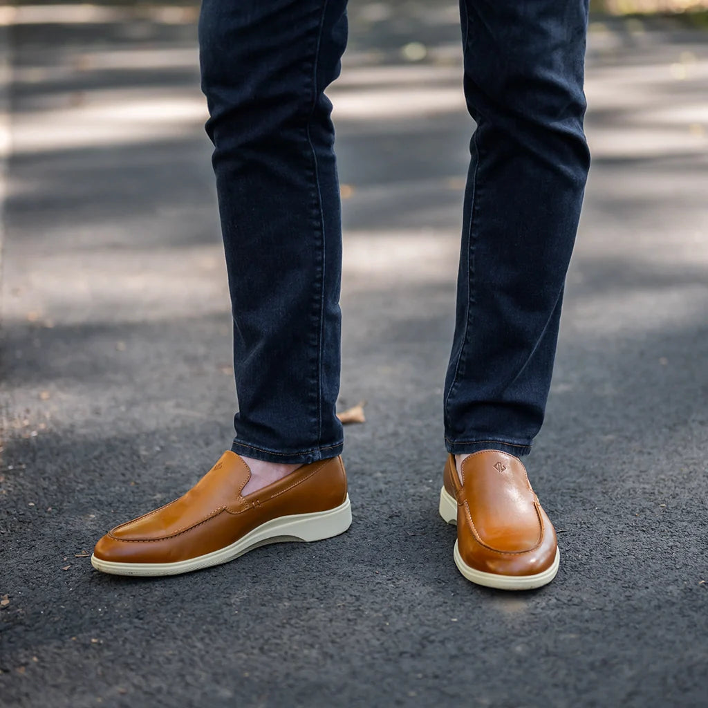 Brown loafers worn with dark jeans on a blurred street background