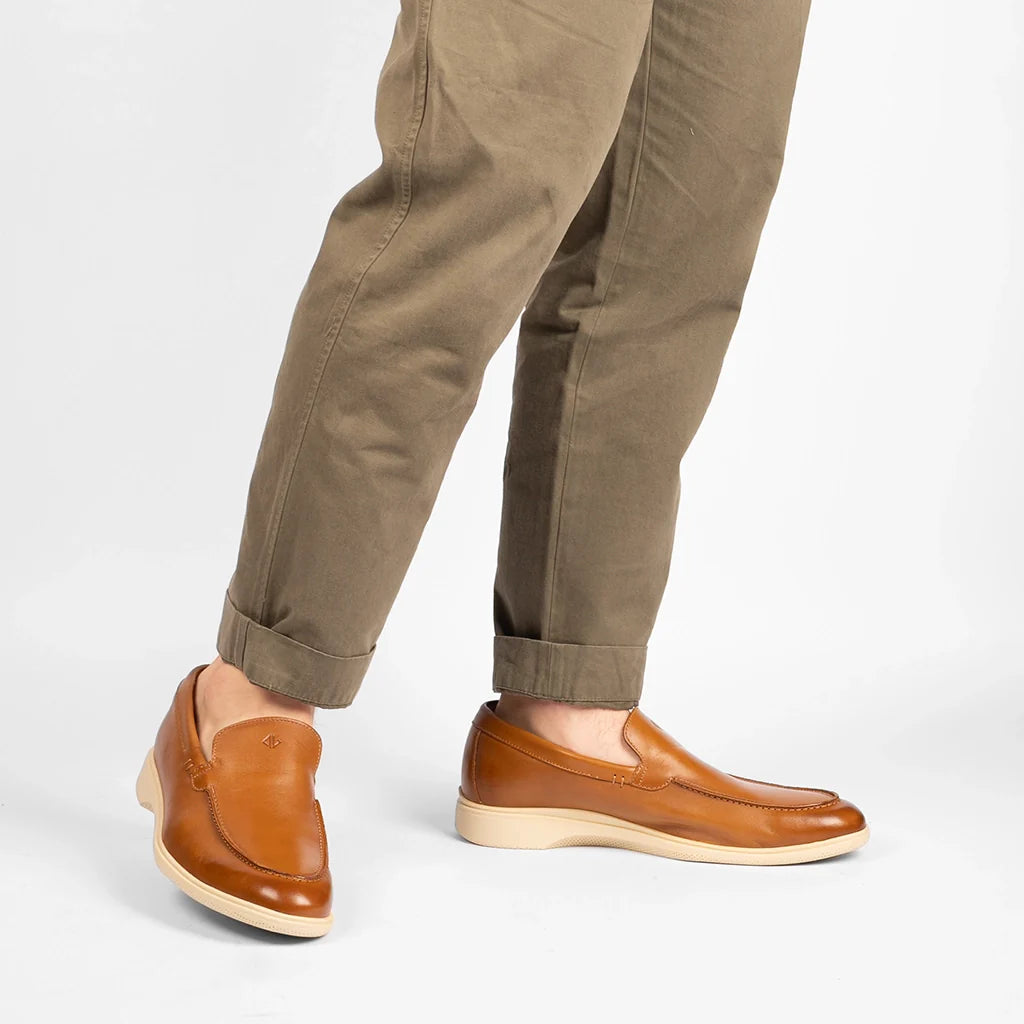 Brown leather loafers worn with beige pants on a white background