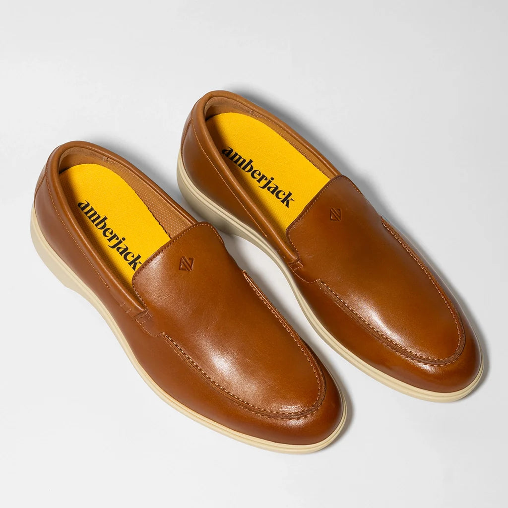 Pair of brown loafers with yellow interior on a light gray background