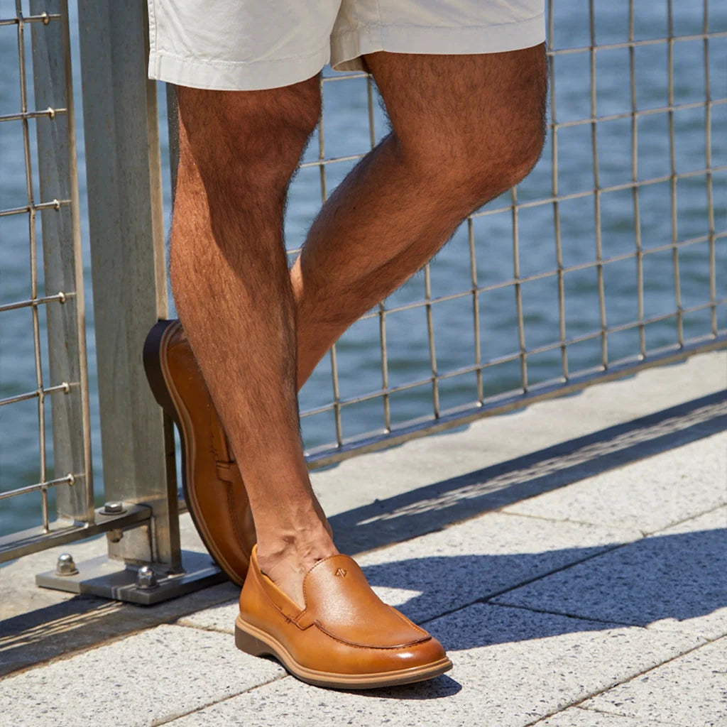 Person wearing brown leather shoes by a waterfront.