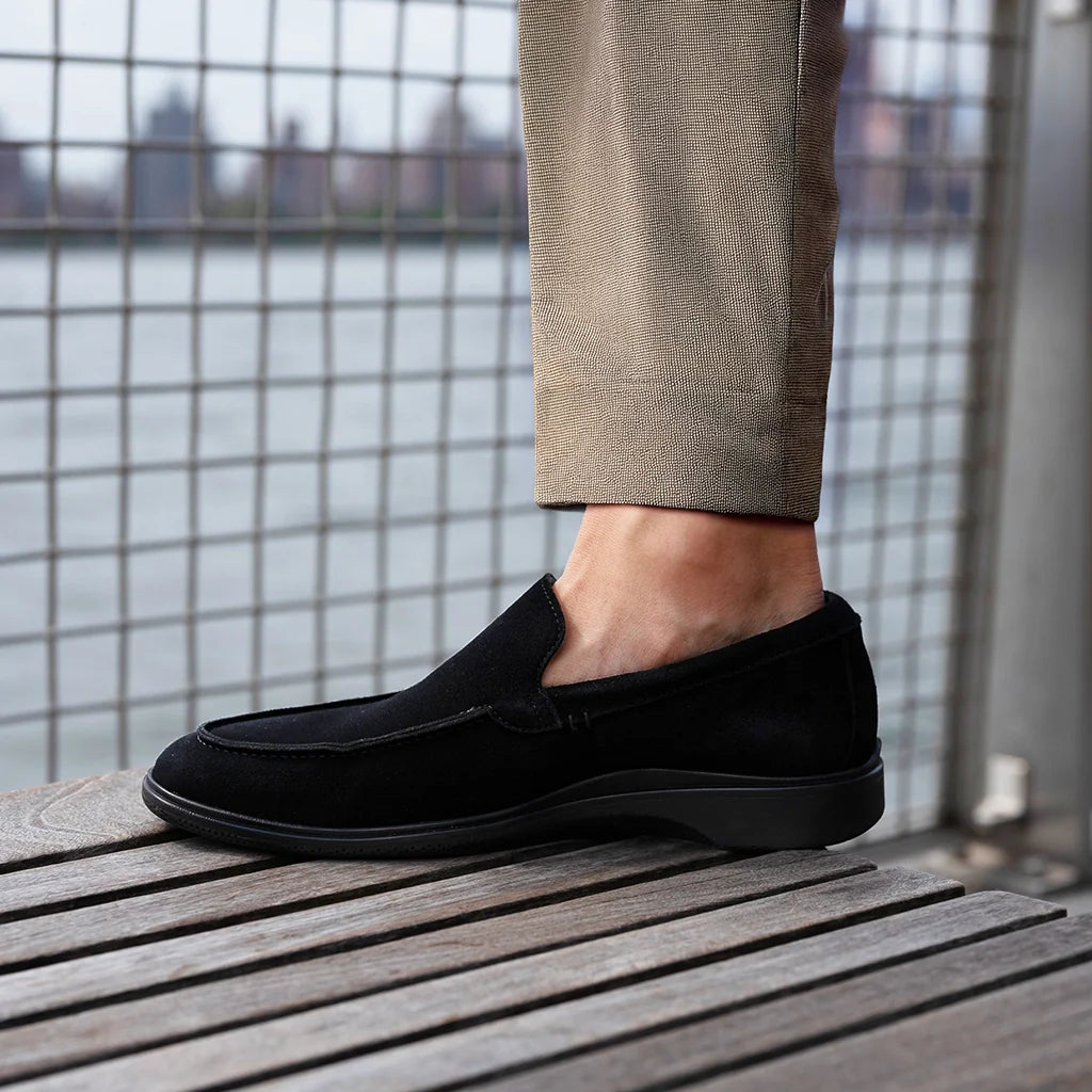 Person wearing black loafers on a wooden surface with a cityscape background