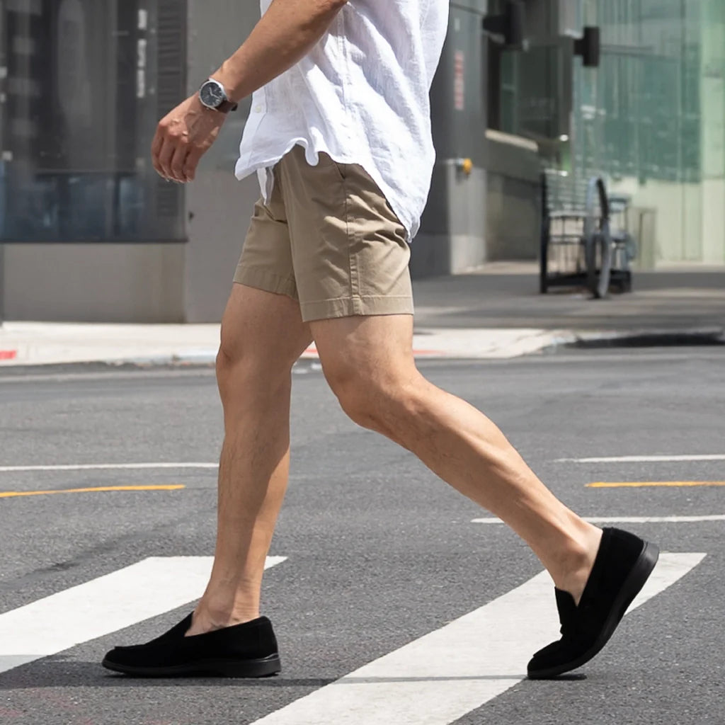 Person wearing beige shorts and black shoes walking on a city street.