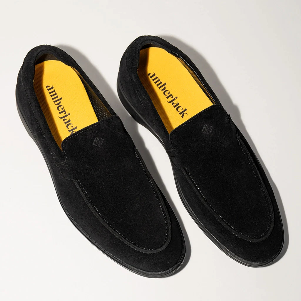 Pair of black loafers with yellow interior on a light gray background