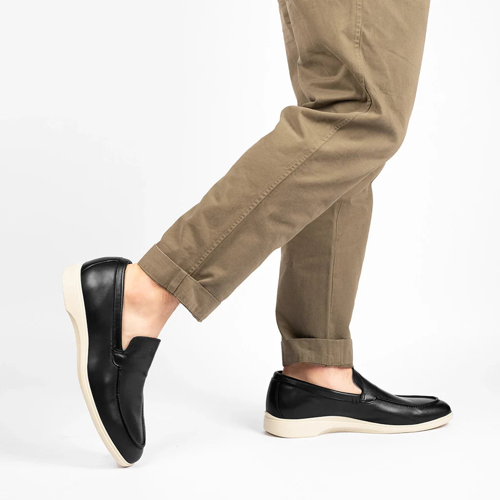 Person wearing black loafers and beige pants on a white background