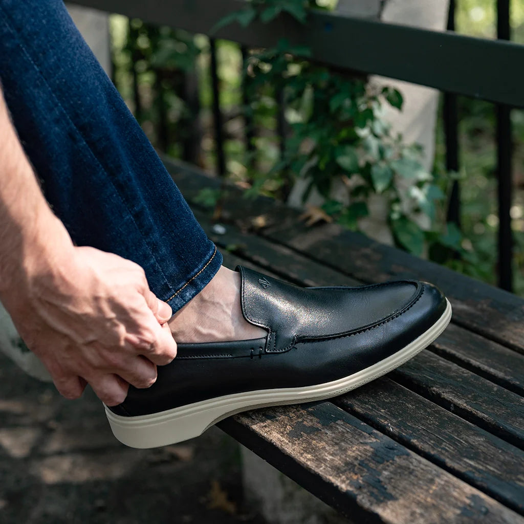 Person wearing a black loafer shoe on a wooden bench with a blurred green background
