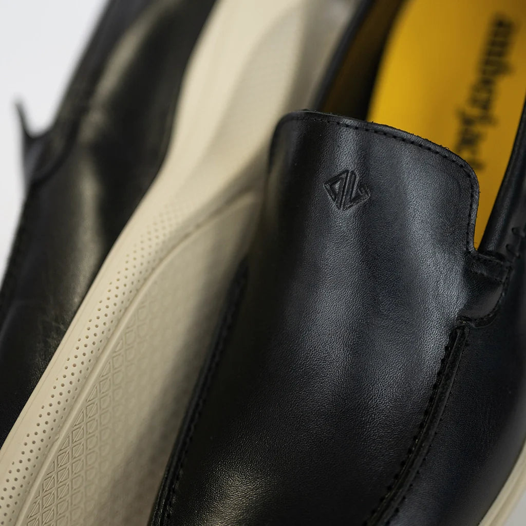 Close-up of black leather shoes with a brand logo on a white background