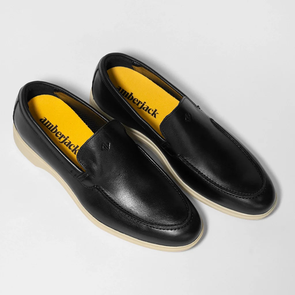Black leather loafers with yellow lining on a light gray background