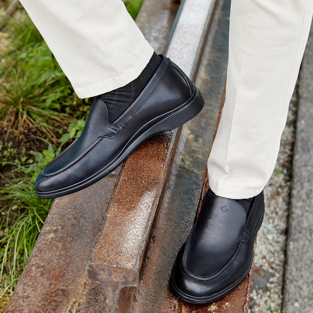 Black dress shoes worn with white pants on a metal railing.