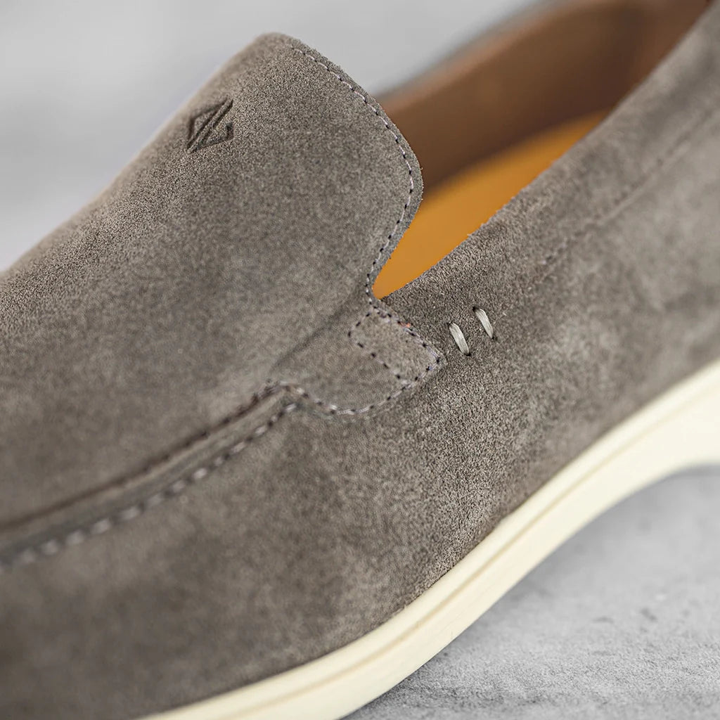 Close-up of a gray suede shoe with a brand logo on a light gray background