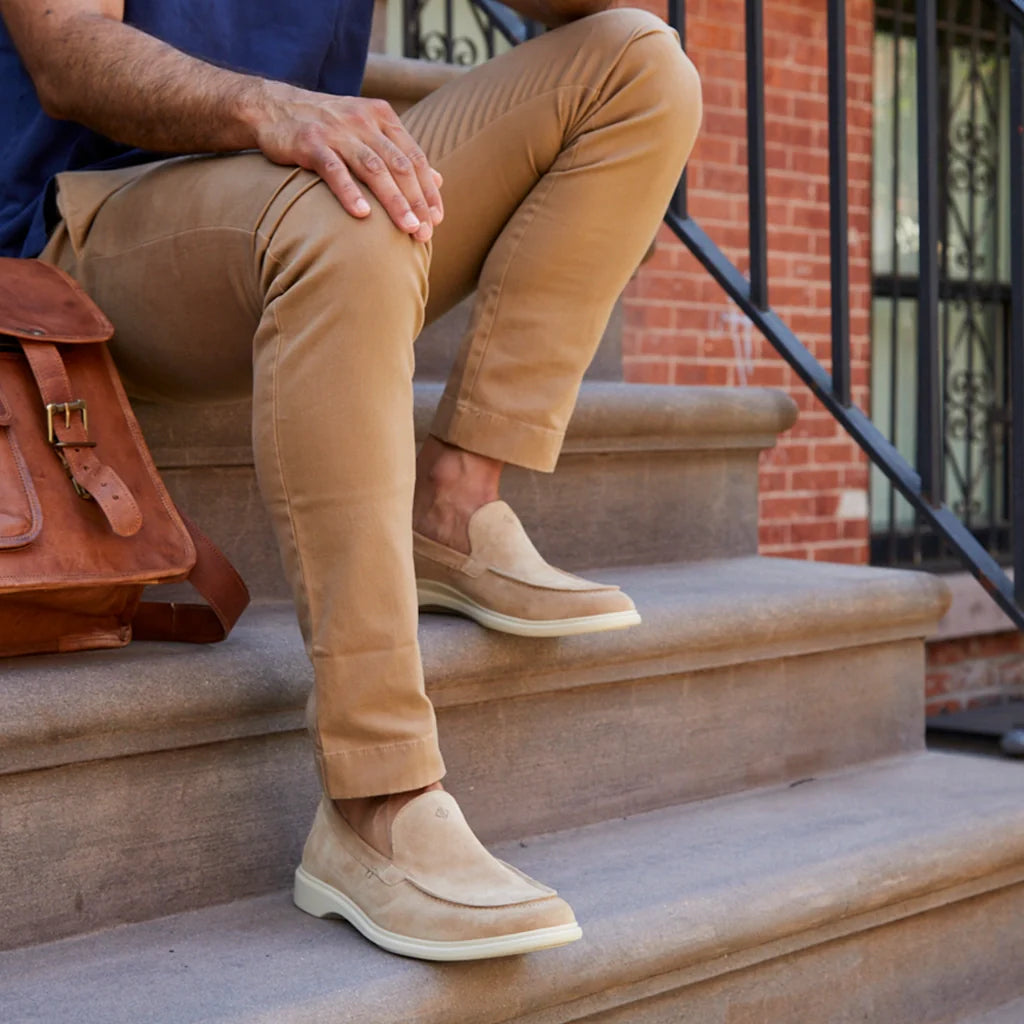 Person wearing beige shoes and tan pants sitting on steps with a brown leather bag.