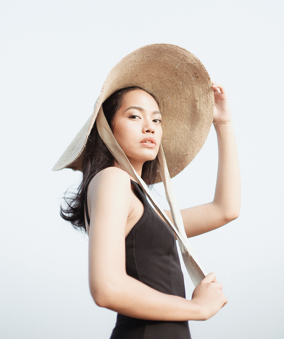 Woman wearing a large straw hat against a plain background
