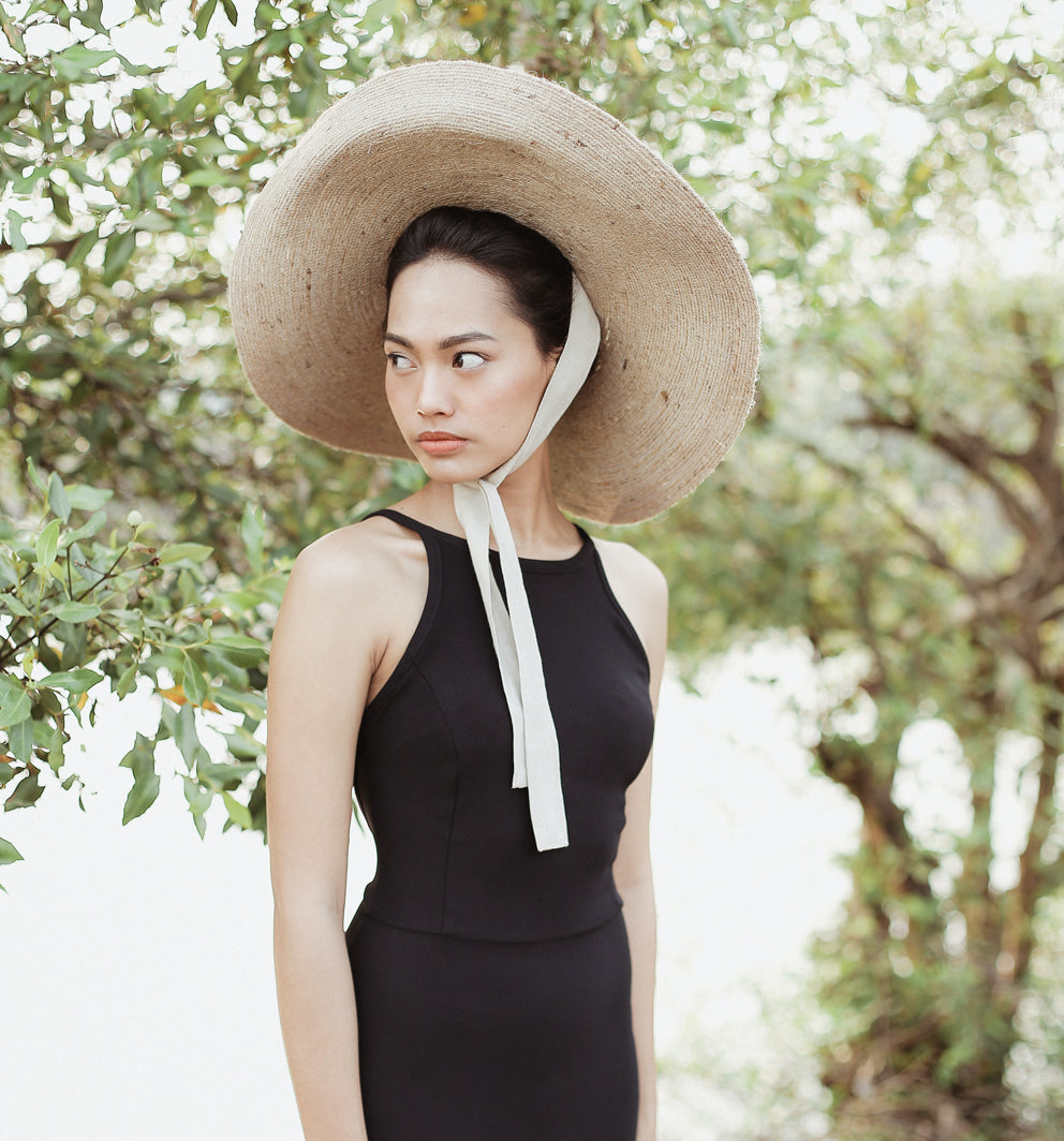 Woman wearing a large straw hat with a white ribbon in a garden setting