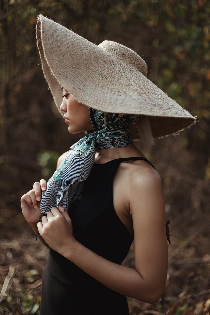 Woman wearing a wide-brimmed hat and patterned scarf in a natural setting