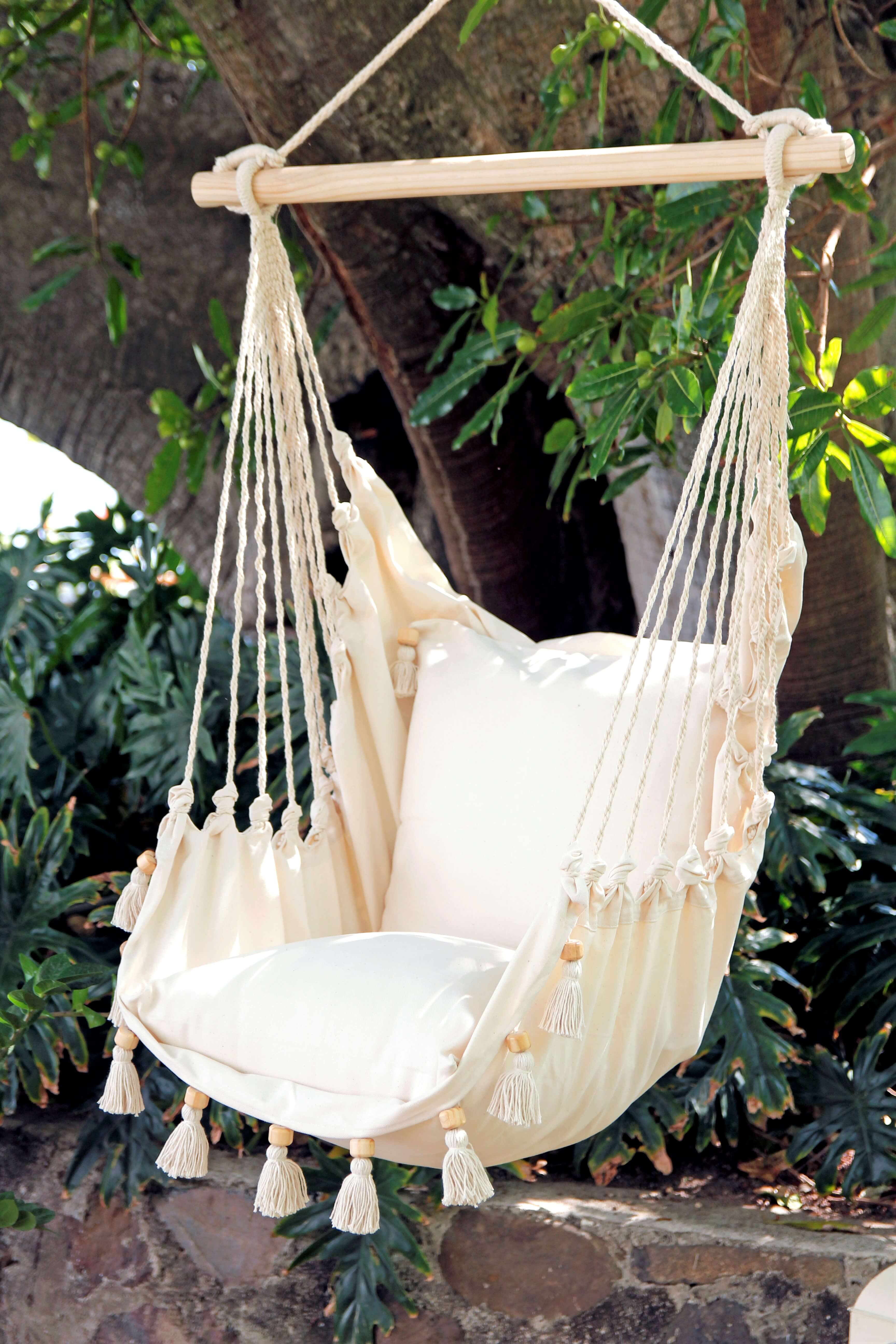 Beige hammock chair with tassels hanging outdoors against a natural background