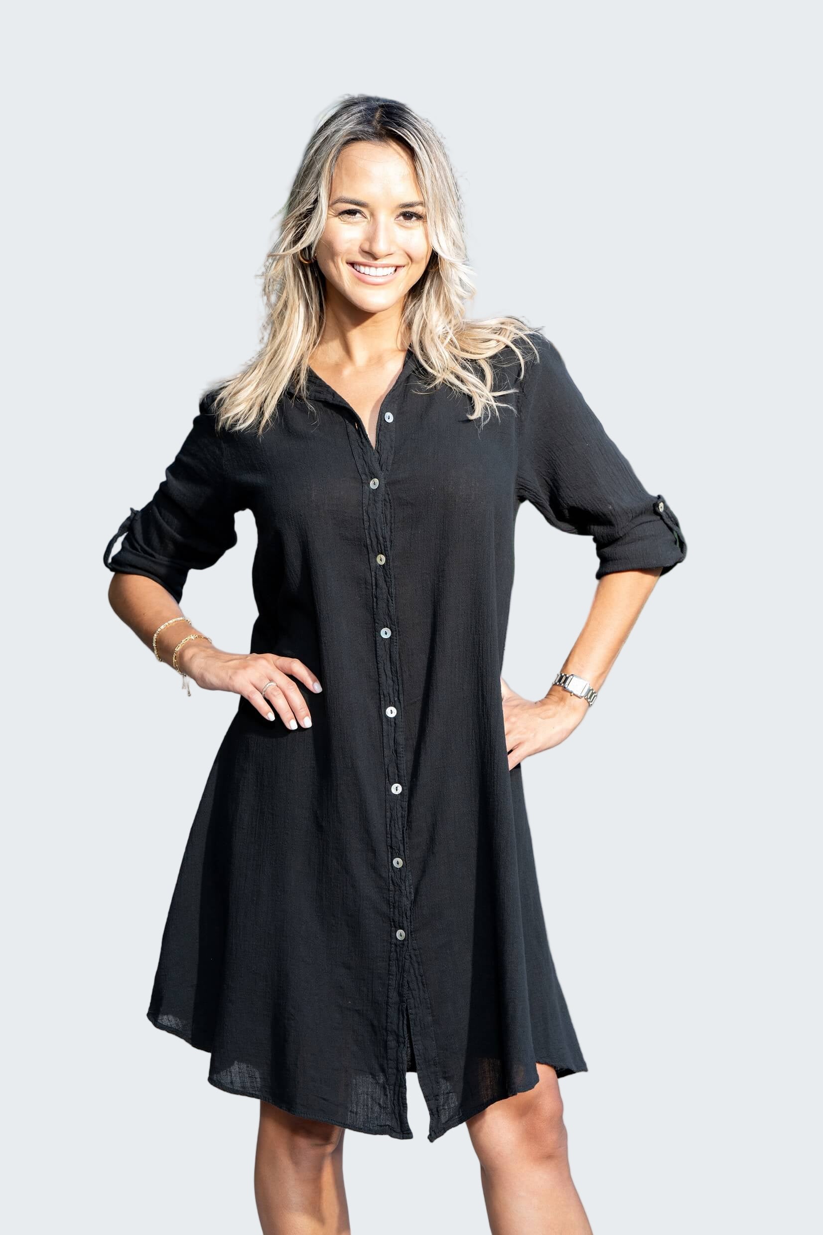 Woman wearing a black dress standing on a sidewalk with cars and trees in the background