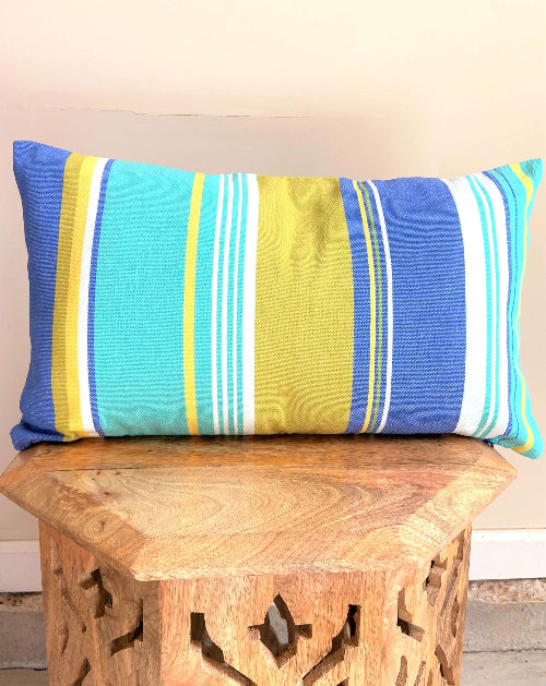 Striped pillow with blue, yellow, and white colors on a wooden bench.
