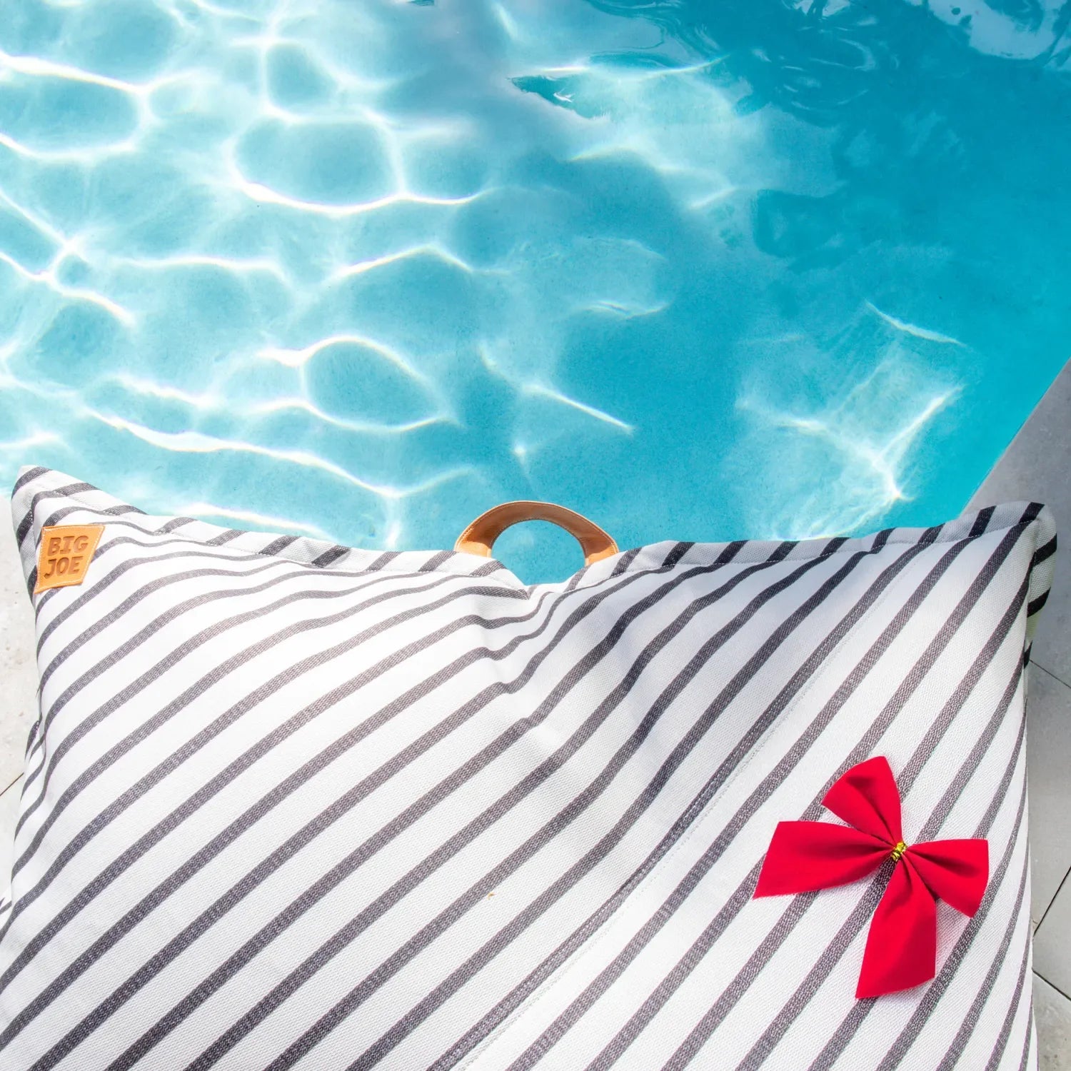 Striped pillow with a red bow by a pool