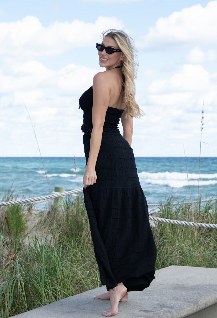 Woman in a black dress standing on a beach with ocean and sky in the background