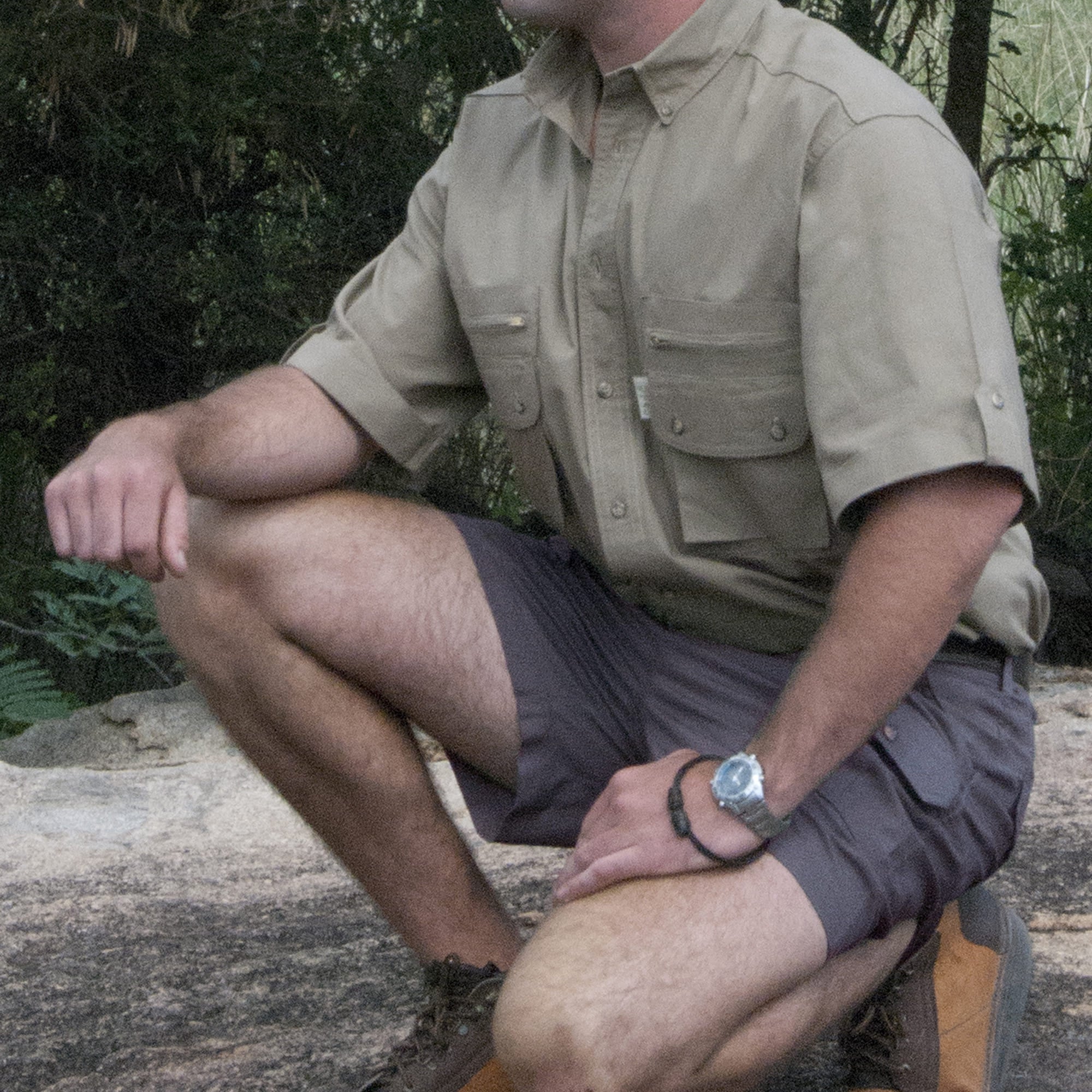Man in beige shirt and gray shorts sitting on a log outdoors
