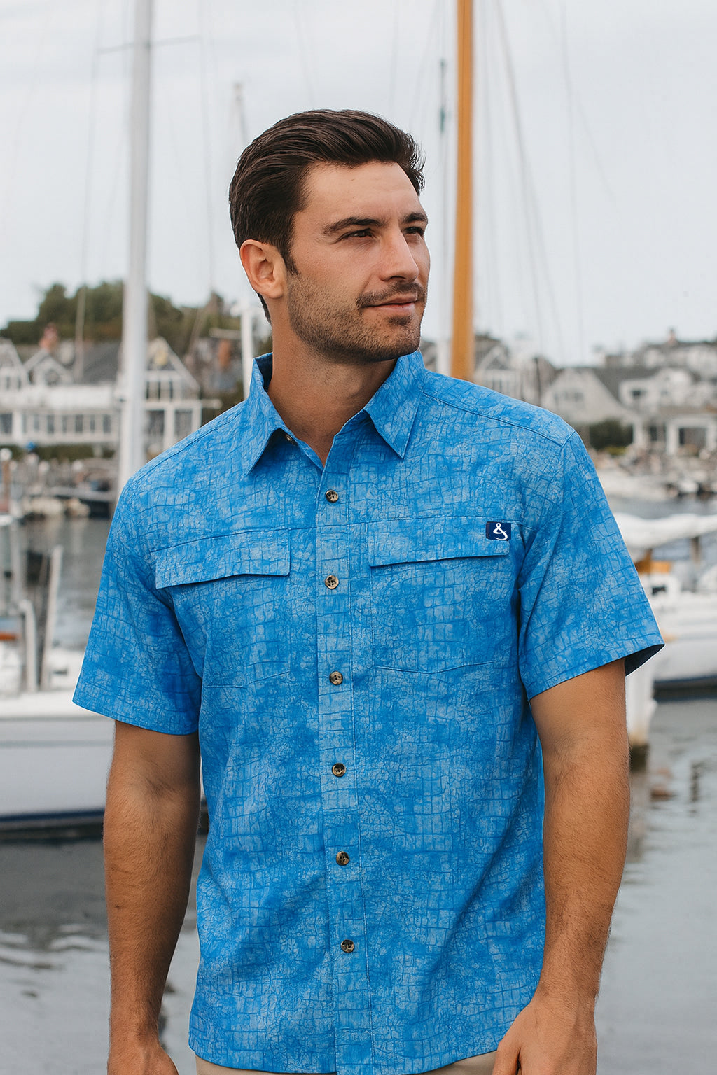 Man wearing a blue patterned shirt standing by a marina