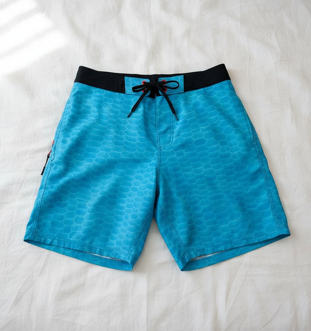 Blue patterned board shorts with a black waistband on a white background