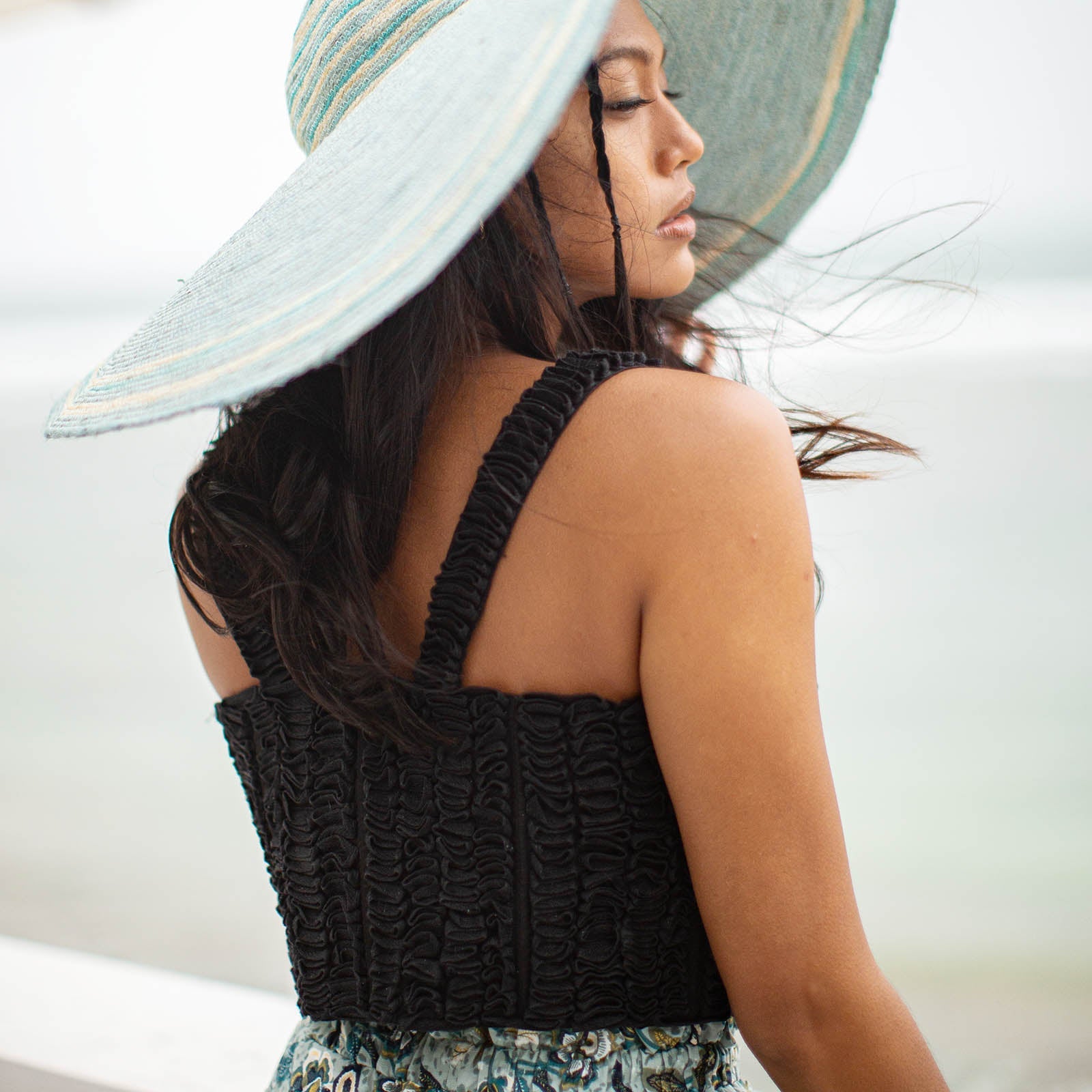 Woman wearing a black crochet top and wide-brimmed hat with a blurred background