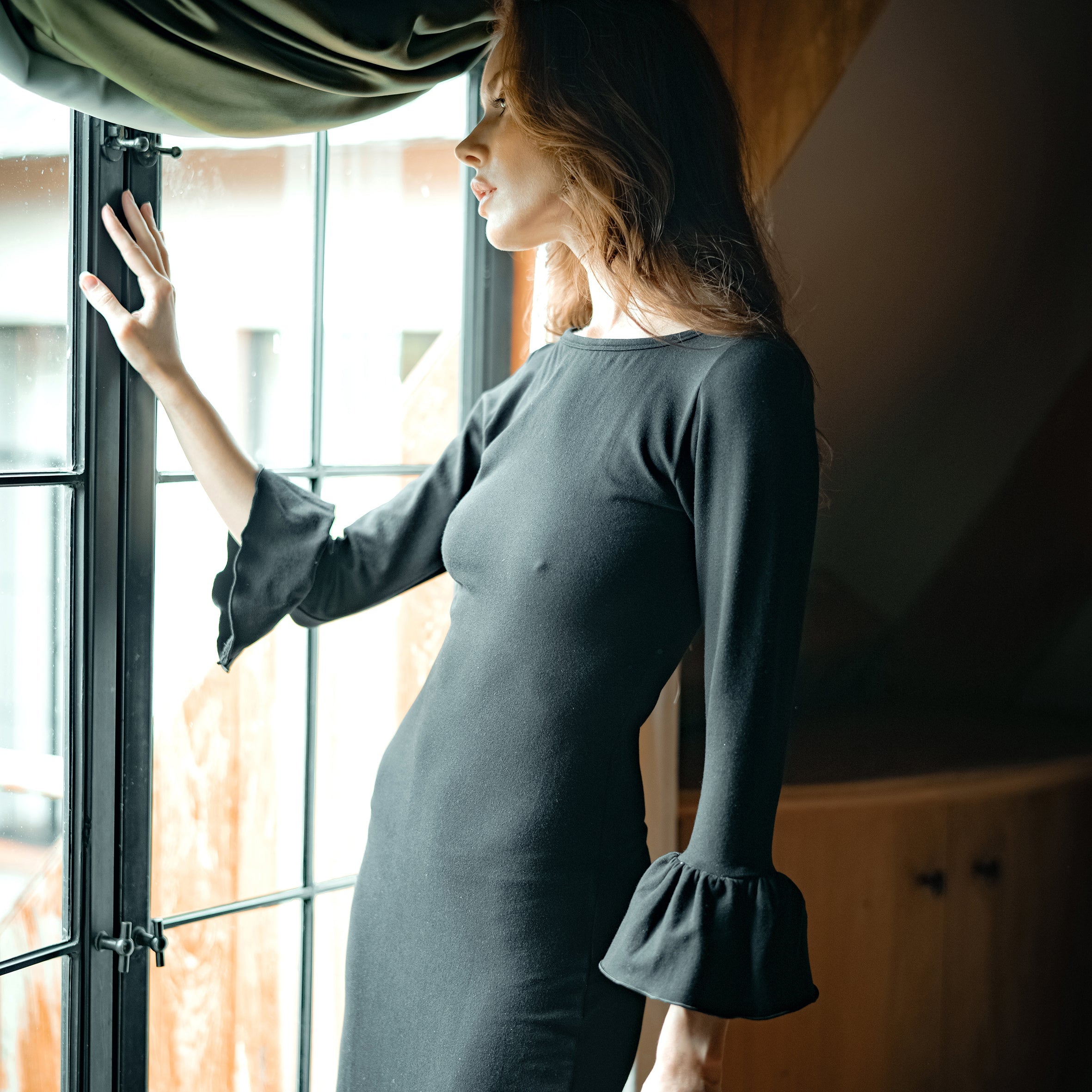 Woman in a dark green dress standing by a window