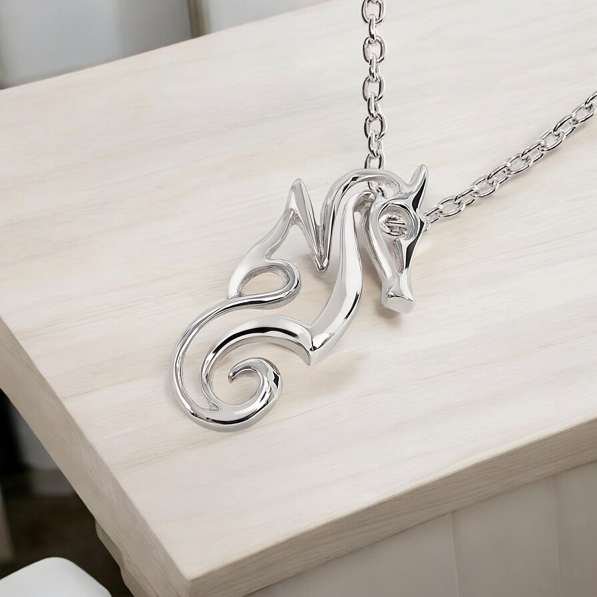 Silver horse-shaped pendant on a chain against a light wooden background