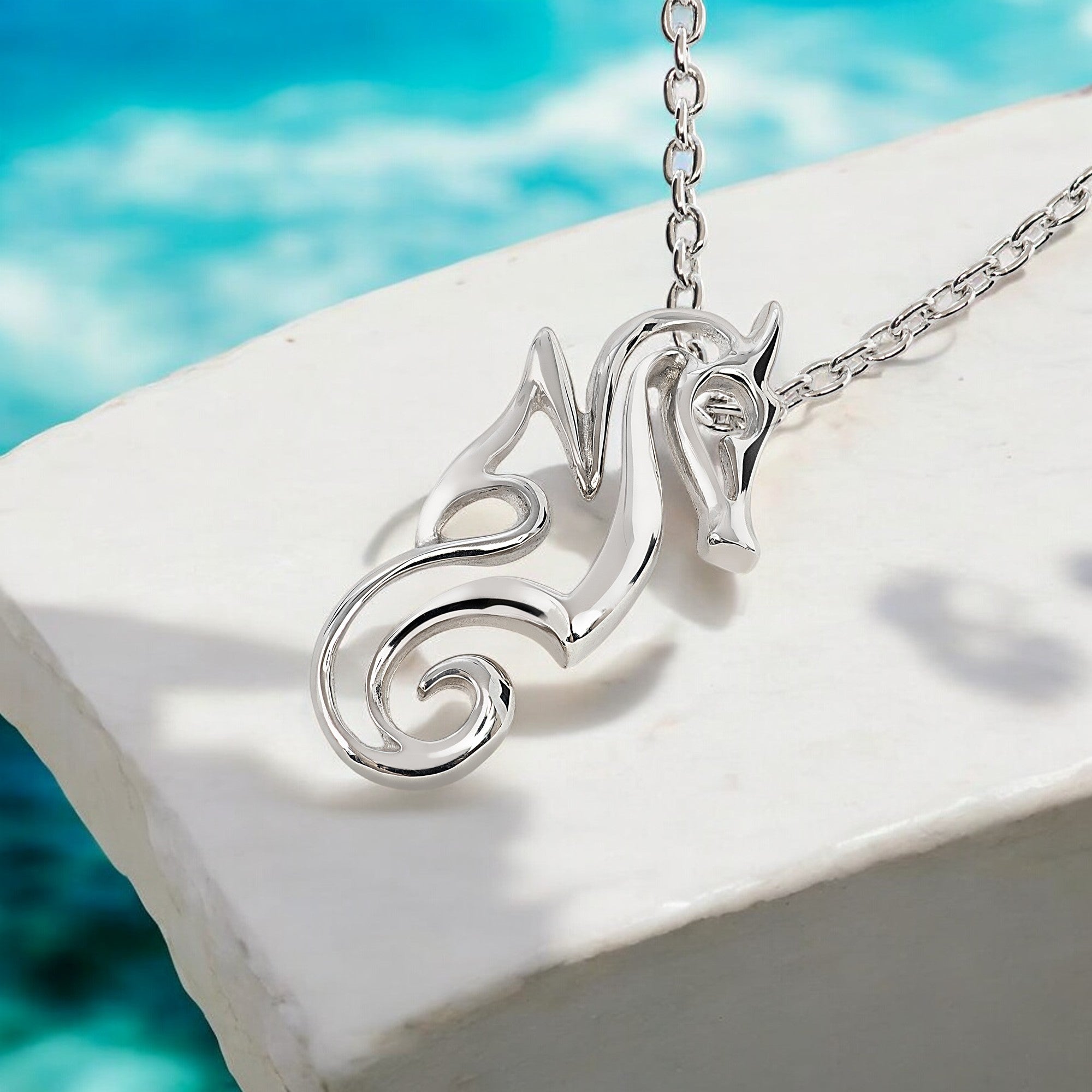 Silver necklace with a decorative pendant on a white ledge with a blue water background