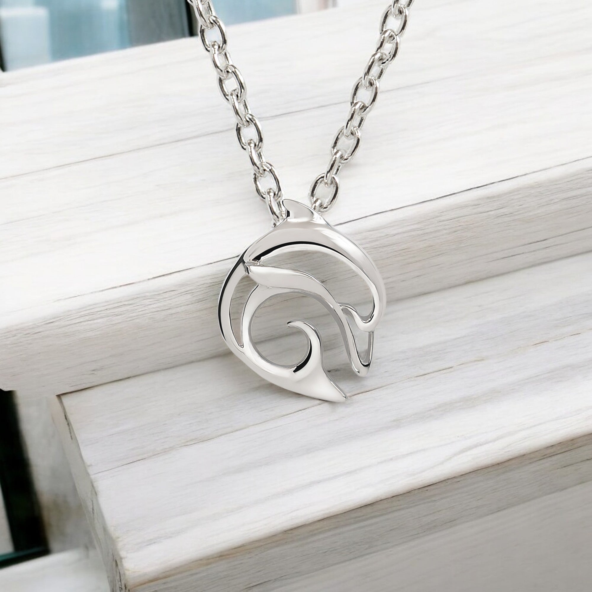 Silver necklace with a wave design pendant on a wooden surface