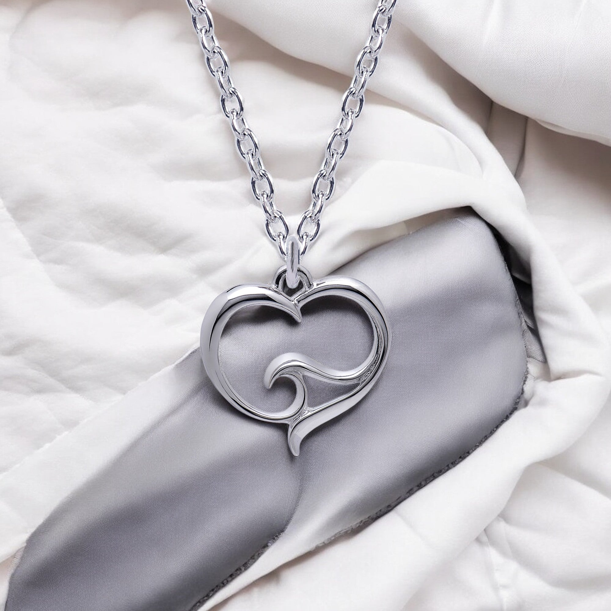 Silver heart-shaped pendant necklace on a white fabric background