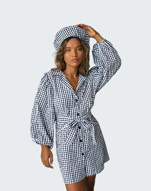 Woman wearing a black and white checkered dress and hat against a plain background