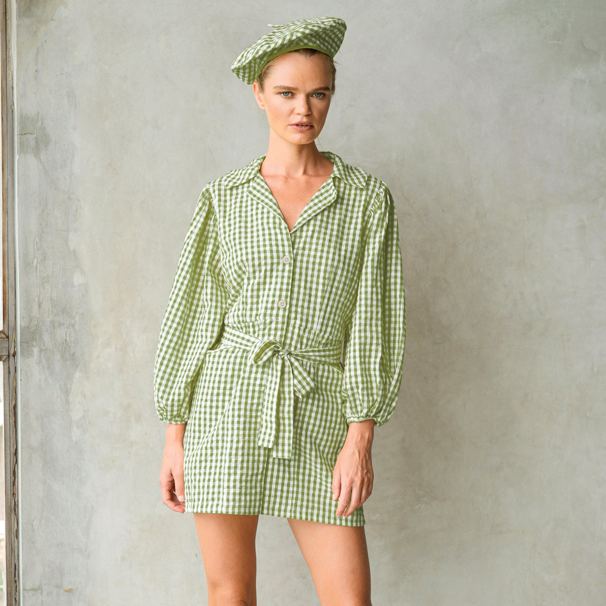 Woman wearing a green checkered outfit with a matching beret against a plain background