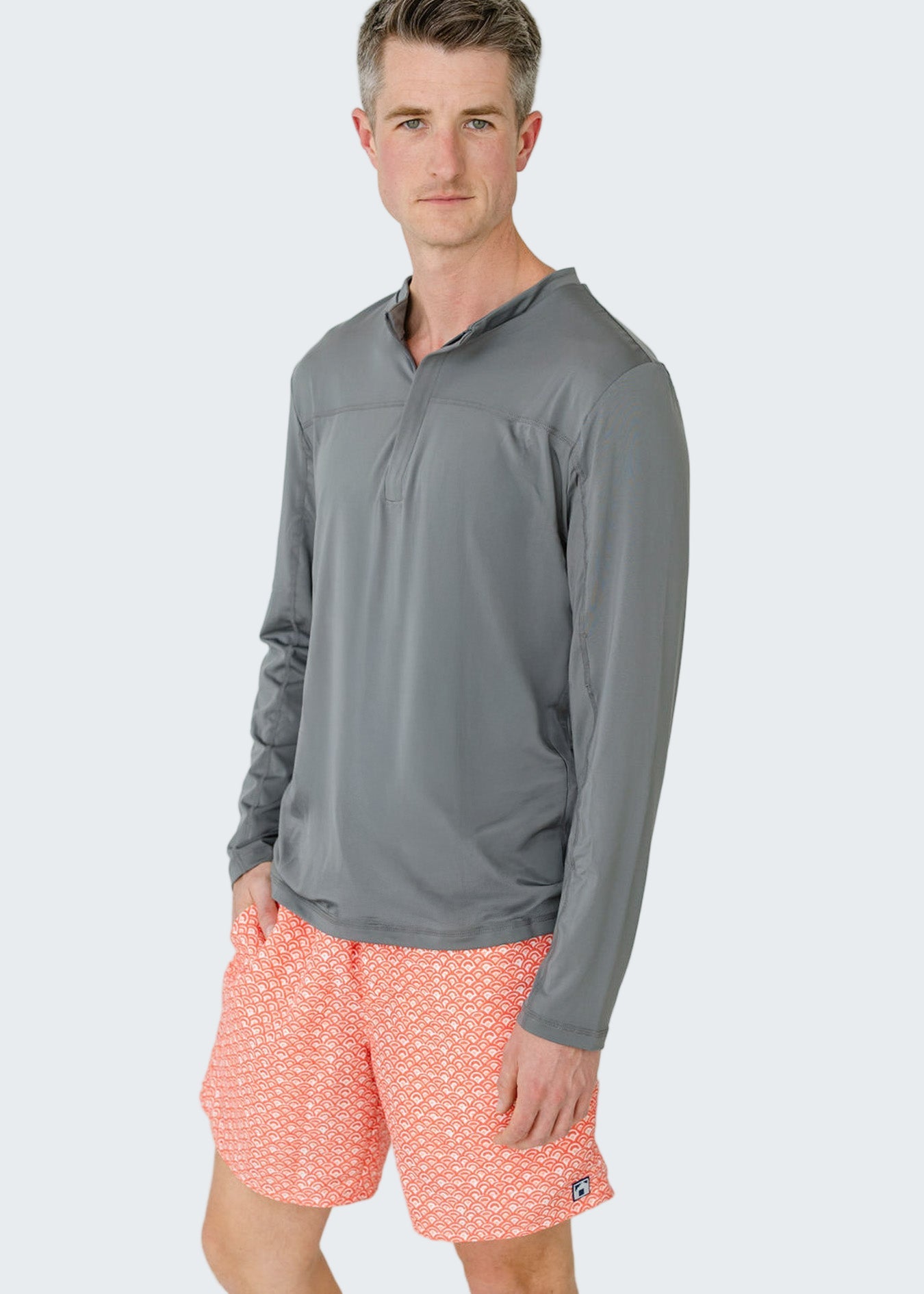 Man wearing a gray long-sleeve shirt and pink shorts with a white pattern on a light gray background