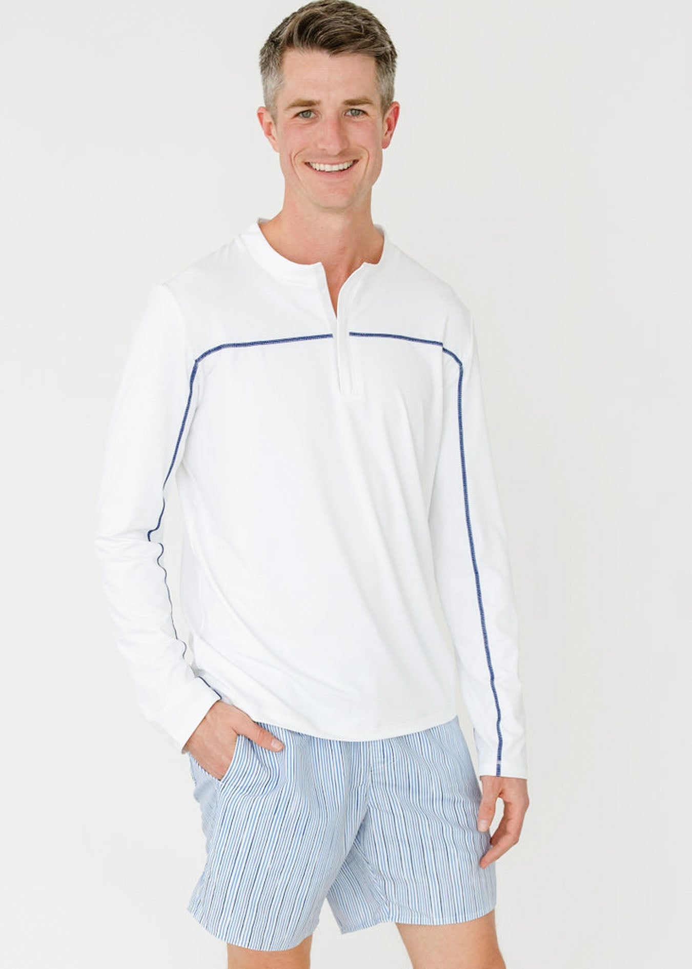 Man wearing a white long-sleeve shirt with blue accents and light blue shorts on a white background