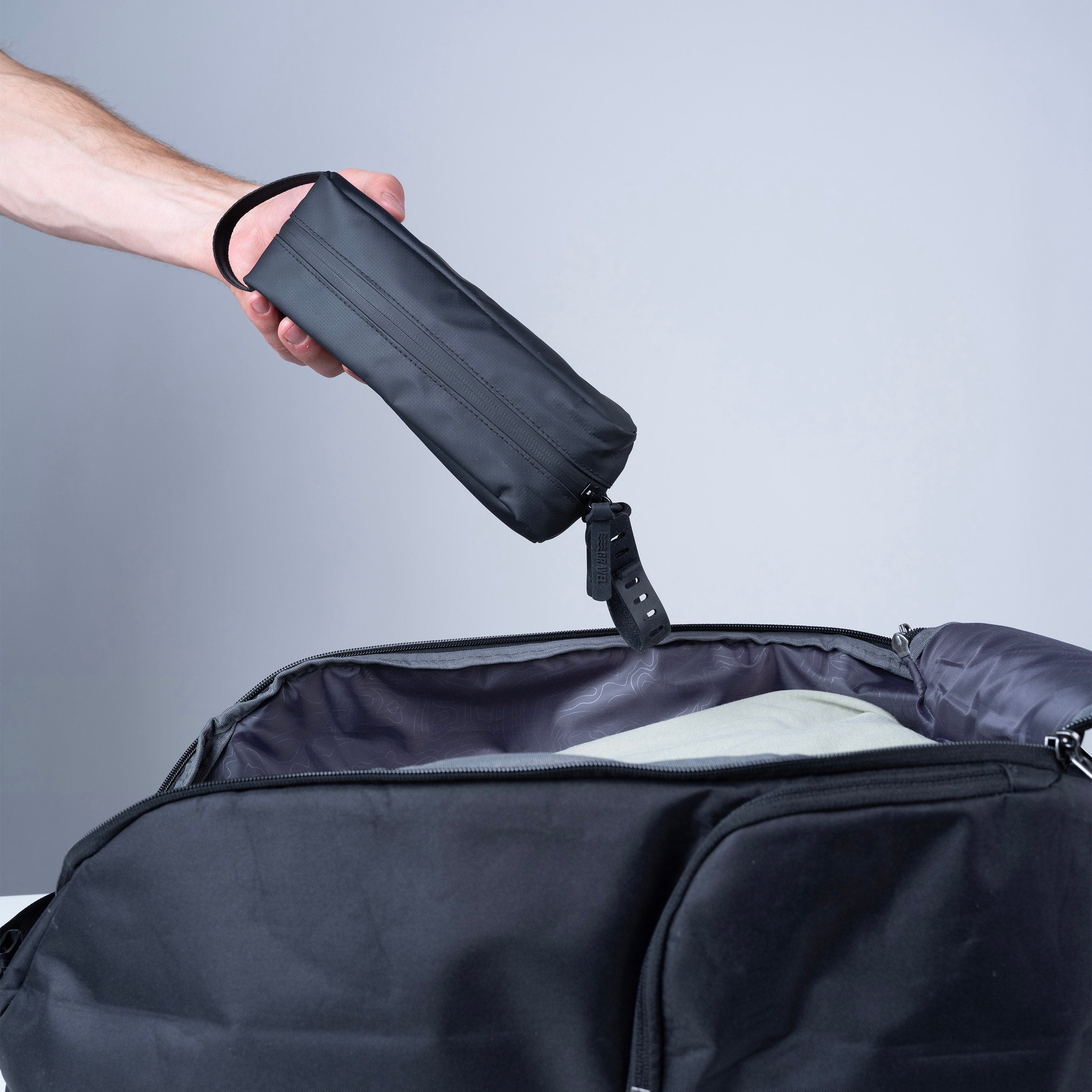Person opening a black suitcase with a smaller black bag being placed inside on a gray background